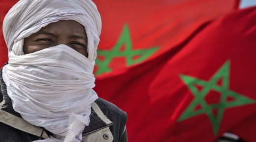 A tribesman stand in front of a Moroccan flags near the border in Guerguerat located in the Western Sahara, on November 26, 2020, after the intervention of the royal Moroccan armed forces in the area. - Morocco in early November accused the Polisario Front of blocking the key highway for trade with the rest of Africa, and launched a military operation to reopen it. (Photo by FADEL SENNA / AFP)