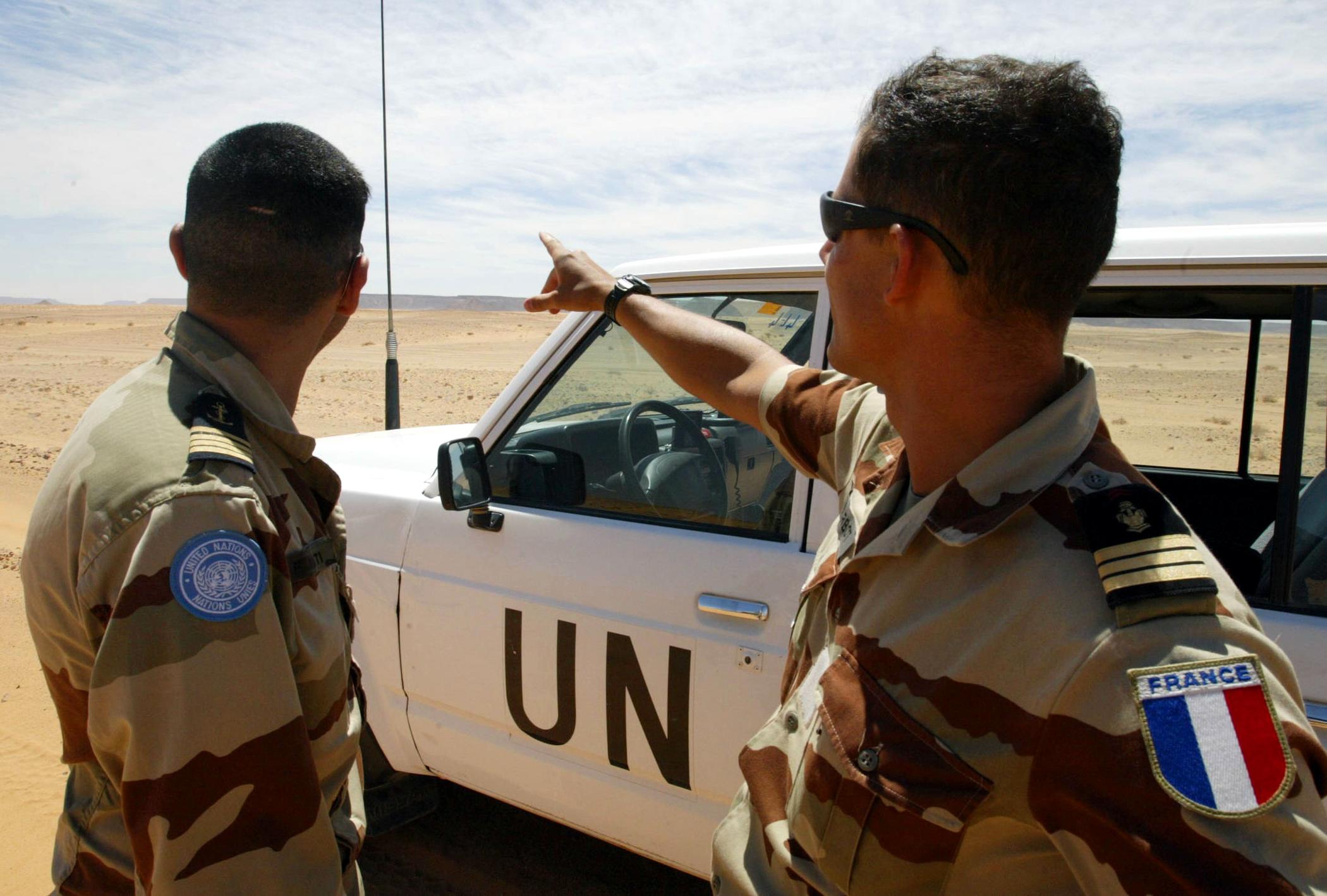French soldiers of the United Nations mission for the organization of a referendum in Western Sahara (MINURSO) watch an almost desert landscape as they stand near their vehicle at the Oum Dreyga observation site, 450 kms south of El Ayoun, the region's main city, 09 May 2004. The Oum Dreyga observation site is one out of nine military sites set up by the MINURSO in 1991, in charge of monitoring a ceasefire reached by Morocco and the Western Sahara's Polisario Front the same year, and one out of four sites on the Moroccan side of a huge, fortified 2,000-kilometer-long sand wall built by the Moroccan army from 1982 to put an end to the Polisario Front's deadly raids. The Polisario Front is a rebel movement backed by Algeria in its fight for independence from Morocco of the former Spanish colony. AFP/PHOTO/ABDELHAK SENNA / AFP PHOTO / ABDELHAK SENNA