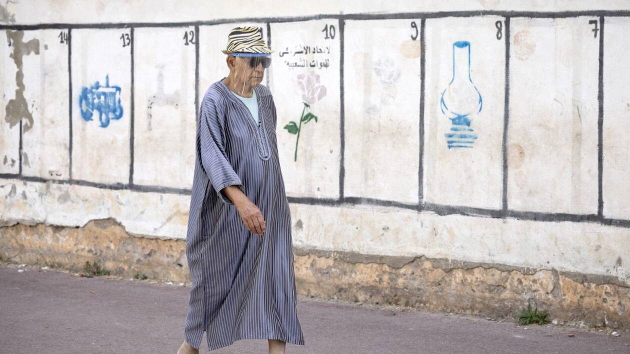 A man walks past a wall on which are painted the symbols of some of the political parties running for the upcoming elections in the Moroccan capital Rabat, on August, 2021. - The electoral campaign for the legislative, regional and municipal elections set for September 8 began today, a day when nearly 18 million Moroccans, are called to vote to elect the 395 deputies of the House of Representatives and the more than 31,000 municipal and regional elected officials, (Photo by FADEL SENNA / AFP)
